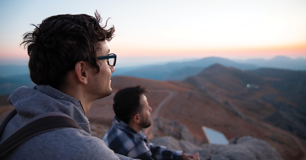 Two men sitting on a mountain top watching the sunrise together