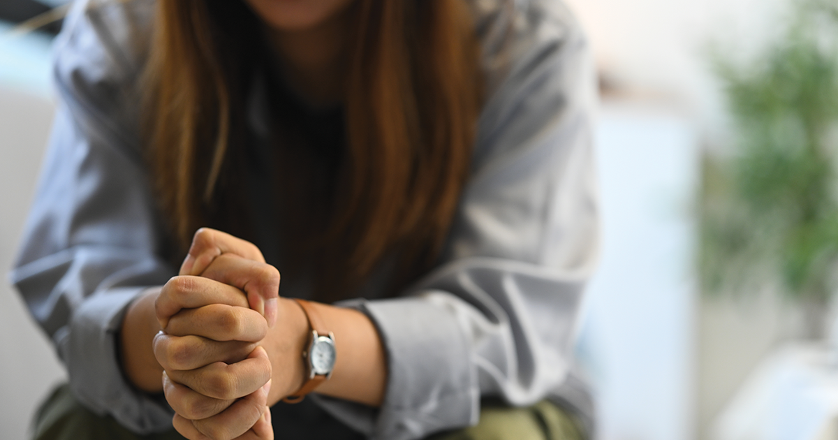 Close-up of woman sitting with hands clasped, appearing thoughtful
