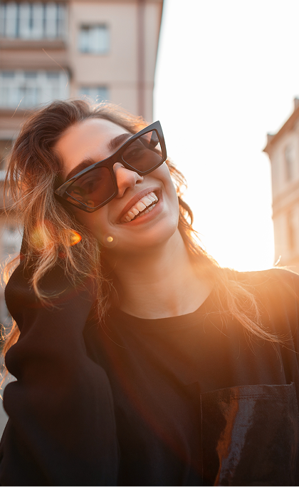 Smiling woman in sunglasses enjoying sunlight outdoors in the city